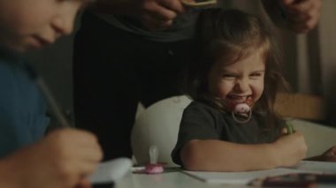 Erkek ve kız kardeş masada kalemlerle birlikte yazıp çiziyorlar. Arkadaş canlısı bir aile. Evde eğitim kavramı.