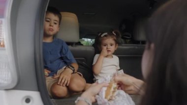 İki sevimli çocuk, modern bir arabanın bagajında oturmuş atıştırıyor ve hafta sonunun tadını çıkarıyorlar. Yolculuk.