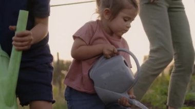 Şirin küçük bir kız bahçede çiçek suluyor, anne babasıyla kardeşine sebze yetiştirmeleri ve eğlenmeleri için yardım ediyor. Etkinlikler