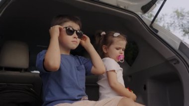 Arabanın arka koltuğunda oturan iki beyaz komik çocuk açık bagajda oynuyorlar. Seyahat konsepti yaşam tarzı. Mutlu aile yolculukları, iki çocuk hayali