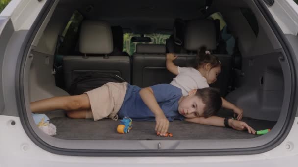 彼女の小さな妹と愛らしい男の子は プラスチックのおもちゃで遊んで車のトランクに座っています 車のコンセプトで旅行する家族旅行 — ストック動画
