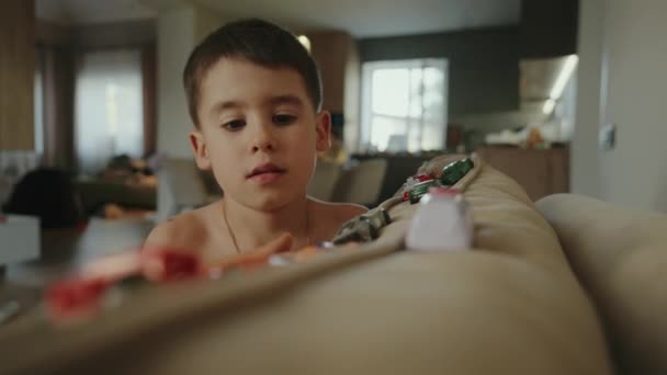Junge Spielt Mit Bunten Spielzeugfahrzeugen Sitzt Auf Dem Sofa Wohnzimmer — Stockvideo