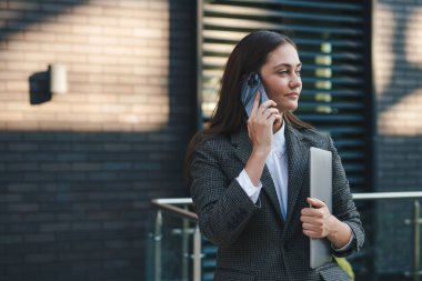 Genç iş kadını elinde dizüstü bilgisayarla şehir dışında konuşuyor. İletişim kuruyorum. Hoş cep telefonu çağrısı.