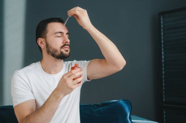 Beyaz bir adam yüzüne kozmetik serumu uyguluyor. Mesaj için yer var. Tımar, aromaterapi ve insanların konsepti