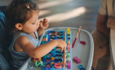 Cute little baby girl sitting in a high chair and plays educational games. Wooden construction set.