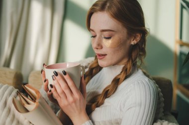Kitap okuyan ve elinde bir kupa sıcak içecek tutan bir kadın. İnsanlar, mevsim ve eğlence konsepti