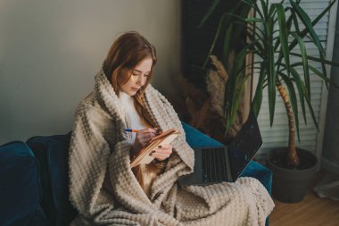 Çekici, genç, kızıl bir kadın kanepede rahat bir şekilde oturuyor, günlük kıyafetler giyiyor ve evdeki deftere bir şeyler yazıyor. Zamanlama hazırlanıyor