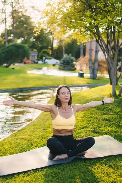Beautiful caucasian fit woman doing breathing yoga exercise in the summer park. Meditation pose, healthcare.