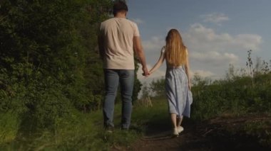 Kırsalda yeşil bir tarlada yürüyen birbirine aşık genç bir çiftin arka görüntüsü. Yaz tatili, seyahat..