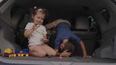 Yol kenarında araba bagajında oynaşan sevimli neşeli erkek ve kız kardeş oyunu, aile tatili konsepti..