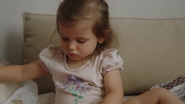 彼女が彼女の手に握っている赤い糸の結び目を解き放とうとソファに座っている赤ちゃんの少女 — ストック動画