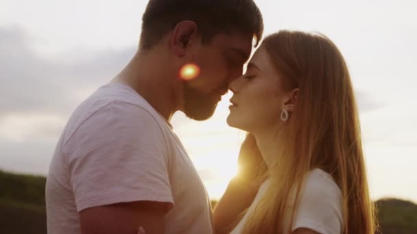 日没の夕方に夏の日にキスするカジュアルな服で幸せな若い素敵なカップルの側面 一緒に お互いを見つめ合い キスする — ストック動画