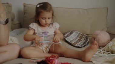 Kanepede oturan, elinde makasla oynadığı ipliği kesen sevimli küçük kız..