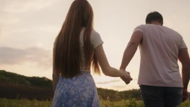 Tanımlanamayan mutlu genç çiftin birbirini kucaklamasının ve yaz akşamları çayırlarda yürümesinin arka görüntüsü. Sevgi dolu bir adam ve kadın.