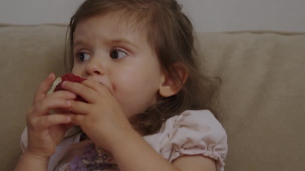ソファーに座って赤いリンゴを食べている小さな女の子 健康的な食事 — ストック動画