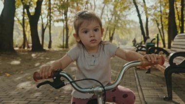 Küçük kız parkta bisiklet sürerken dengesini korumayı öğreniyor. Çocukluk rüyası. Hafta Sonu.