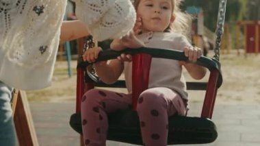 Tanımlanamayan anne salıncakta sallanan küçük kız, dışarıda oyun oynayan sevimli kız. Annemle hafta sonu. Anne ve çocuk için etkinlikler.