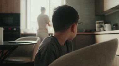 Küçük çocuk, annesi mutfakta yemek pişirirken onun okulda nasıl olduğunu konuşuyor..