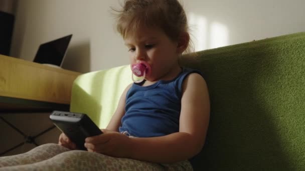 ソファーに座っているハンドヘルドゲームコンソールをプレイする小さな赤ん坊の少女 ポータブルゲームコンソール ビデオゲームの時間 ゲームパッドで遊ぶ — ストック動画