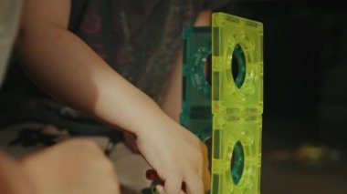 Çocuk ellerinin evde yerde oturup manyetik oyuncaklarla oynadığı yakın plan görüntüler. Bloklardan inşa edilen çocuklar. Kardeşler dostluğu.