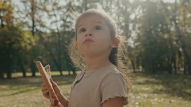 Elinde bir dilim ekmek olan beyaz bir kız, sonbahar parkında yürüyüş yaparken eğleniyor. Mutlu çocukluk özgürlüğü kavramı.
