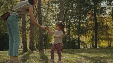 Anne küçük kızına meşe palamudunu nasıl tekmeleyeceğini gösteriyor. Sonbahar parkında birlikte oynamak, oyun uydurmada yaratıcı olmak.