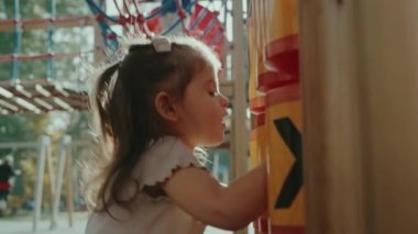 Oyun parkında sarı ekipmanlarla oynayan küçük bir kız. Yaz parkında tek başına oynayarak mutlu olmak. Çocuk parkındaki çocuklar. Yaz tatili eğlencesi.