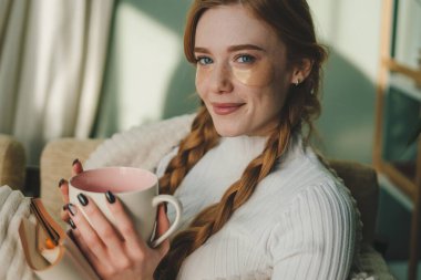 Oturma odasında bir fincan kahve ya da çay içip hafta sonları battaniyenin altında eğlenen genç bir kadın hayal et. Kahve molası, rahatlama konsepti.