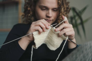 Ellerinde el yapımı eşyayla kanepede oturan hoş kıvırcık saçlı bir kadının portresi yün iğneli sıcak eşarp örmenin keyfini çıkarıyor. Boş zaman hobisi