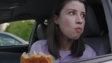 Trafik sıkışıklığından dolayı sabah sabah trafik sıkışıklığında bekleyen bir kadın arabada hamburger yiyor. Fast food arabada. Trafik sıkışık..