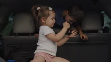Arabaların bagajında oturan sevimli küçük çocuklar aile yolculuklarına başlamak için su içiyorlar. İki mutlu çocuk, erkek ve kız. Aile arabası bagaj bölmesi