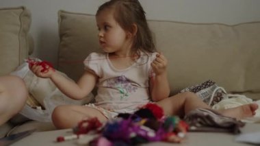 Bebek kız önünde renkli örgü ipliklerle kanepede duruyor, onları elinde tutuyor ve onlarla oynuyor. Ev eğlencesi konsepti.