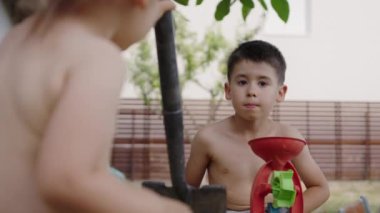 Kız kardeşiyle çamurlu su birikintilerinde oynayan sevimli beyaz çocuk arka bahçedeki ev bahçesinde oyuncak inşaat makineleriyle oynarken kirleniyor.