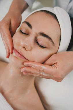 Güzellik uzmanlarının elleri, güzellik salonunda cilt bakımı yaparken hastanın yüzünü köpükle yıkıyor. Nemlendirici krem, masaj yüzü. Günlük spa sabahı