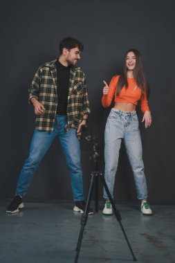 Genç, gülümseyen bir çift evde dans ederken video kaydediyor, eğleniyor, cep telefonu kamerasında poz veriyor, sosyal ağlar için içerik yaratıyor, akıllı telefon kullanıyor.