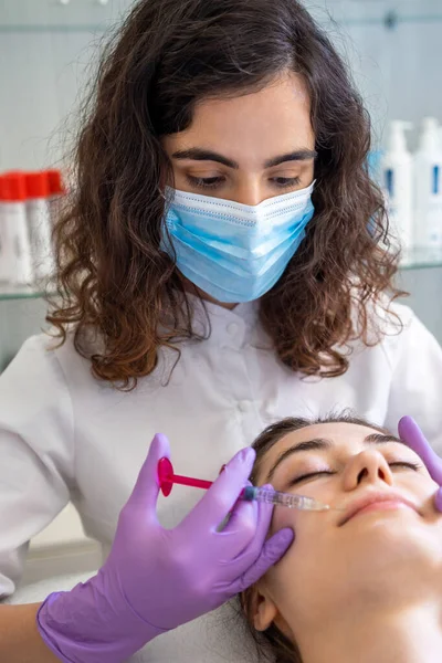 Doctor with medical mask making lip augmentation procedure of a beautiful woman in a beauty salon. Cosmetology skin care.