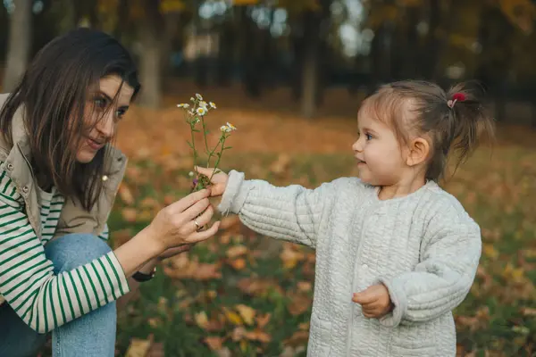 Küçük kız annesine papatya çiçeği veriyor. İkisi de mutlu, bağlı ve ait görünüyorlar. Birbirinize bakın.