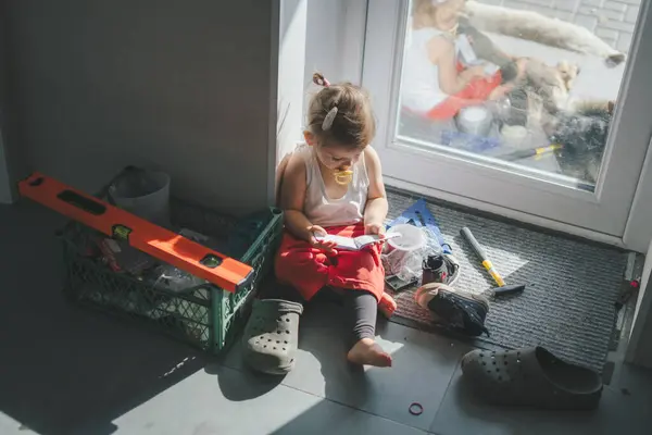 Adorable little girl sitting on the floor in the house among construction tools. The profession of an engineer for a child.