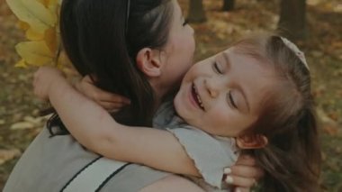 Kızı annesine sıkıca sarılıyor, sonbahar parkında eğleniyor. Aile tatilde gün batımında birlikte vakit geçirir. Sonbahar tatili kavramı.