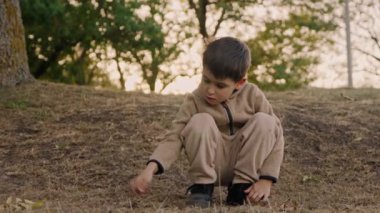 Çocuk bir sopayla eğilip oyun oynuyor, toz yapıyor. Çocuklar için etkinlik. Çocuklu aileler için açık hava eğlencesi