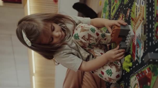 リビングルームの床で玩具のコンストラクターを演じているおかしい女の子 おもちゃの街を建てます ホームレジャー 遊び時間 教育興味深いボードゲーム — ストック動画