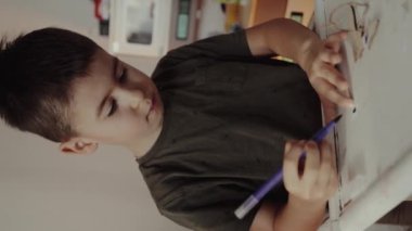 Kafkasyalı küçük çocuk sağ elinde bir kalem tutuyor ve masasında çizim yapıyor. Eğitim kavramı.