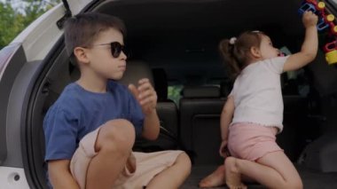 İki mutlu çocuk bir arabanın bagajında birlikte oturup aile arabasının bagajında oynuyorlar. Hafta sonu seyahati ve tatil konsepti.