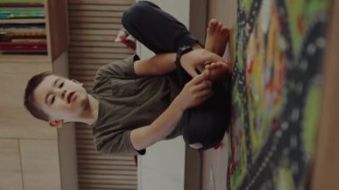 Beyaz tenli küçük bir çocuğun evde tek başına oturup oynadığı geniş bir manzara. Ön manzara. Oynamak, eğlenmek, eğitim kavramı.