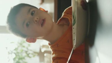 Mutfak masasında oturmuş, kameraya bakıp sağlıklı bir yemek yiyen sevimli küçük bir çocuğun portresi. Sağlıklı ve lezzetli..