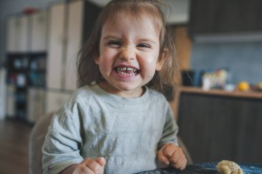 Annesinin mutfakta yemek yapmasına yardım ederken kameraya gülümseyen küçük kız. Çocuklar hamur köftesi pişirir.