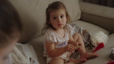 Annesinin yanında oturan, dikiş işi için makas ve malzeme kullanan sevimli beyaz bir kız. Kendi elleriyle bir ürün yaratıyor. Çocuk öğreniyor.