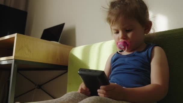 白人ベビーガールは 家庭でソファーでスマートフォンゲームを使用して太鼓を鳴らします ベビーテクノロジーライフスタイルコンセプト — ストック動画
