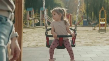 Sevimli kız salıncakta sallanıyor annesiyle parkta oyun parkında eğleniyor. Mutlu bir çocukluk. Çocuk, küçük kız. Mutlu bir aile. Aile kavramı
