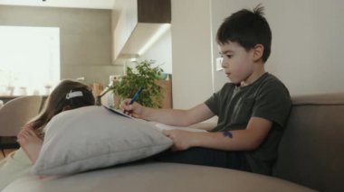 Alfabe yazan küçük çocuk çok mutlu görünüyor, evdeki kanepede rahat oturuyor. Eğitim, aile ve ev ödevi kavramı.